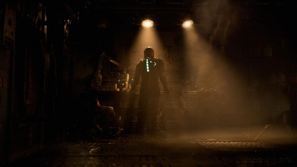 Isaac Clarke, the protagonist of Dead Space, stands under a spotlight in a dark, dingy corner of a spaceship.