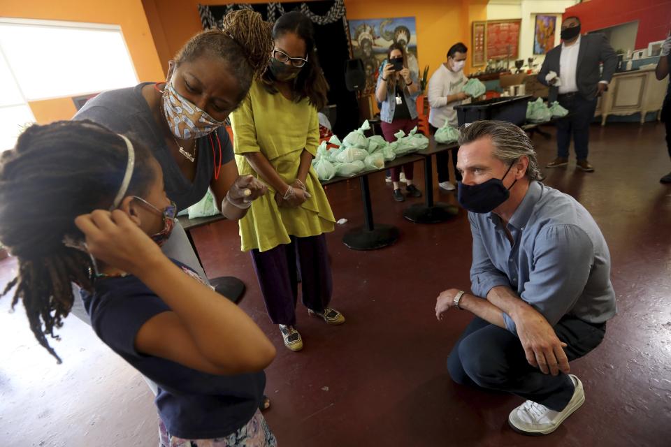 California Gov. Gavin Newsom, right, listens as he is introduced to Kirikou Muldrow, 8, by California Senator Holly Mitchell and California Assembly Member Sydney Kamlager-Dove, right, during a visit to the Hot and Cool Cafe in Leimert Park in Los Angeles on Wednesday, June 3, 2020. The cafe has been providing meals prepared at the establishment three days a week for older adults during the coronavirus pandemic stay at home order. Muldrow has been helping pack the meals. Her mother is co-owner of the the cafe. (Genaro Molina/Los Angeles Times via AP, Pool)