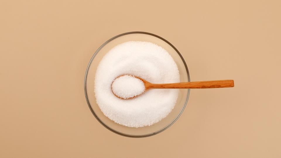 A bowl of Stevia, a gut-friendly sweetener, with a wooden spoon on a beige background