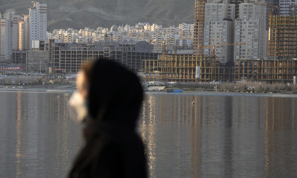 A woman wearing a face mask walks on the shore of the Persian Gulf Martyrs' Lake as residential buildings are seen at rear, in Western Tehran, Iran, Sunday, March 15, 2020. Many people in Tehran shrug off warnings over infection by the new coronavirus as authorities complain that most people in the capital are not treating the crisis seriously enough and many are not taking any preventive measures. (AP Photo/Vahid Salemi)
