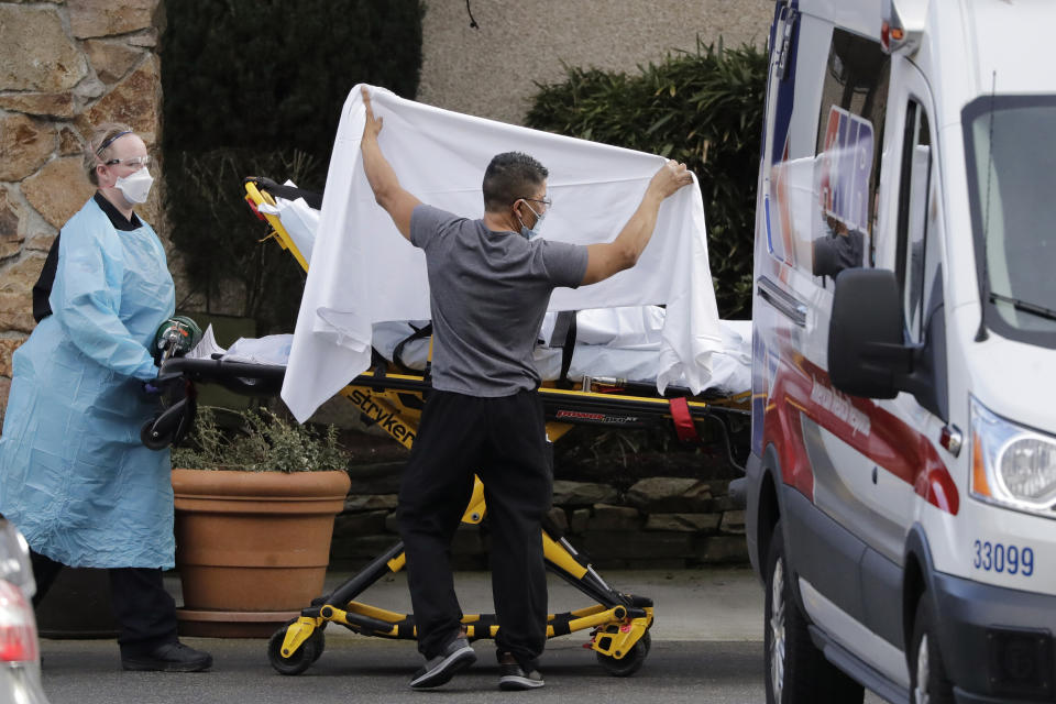 FILE - In this Feb. 29, 2020, file photo, a staff member blocks the view as a person is taken by a stretcher to a waiting ambulance from a nursing facility where people are sick and being tested for the COVID-19 virus in Kirkland, Wash. From Miami to Seattle, nursing homes and other facilities for the elderly are stockpiling masks and thermometers, preparing for staff shortages and screening visitors to protect a particularly vulnerable population from the deadly new coronavirus. (AP Photo/Elaine Thompson, File)