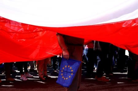 FILE PHOTO: A man holds an EU flag as he stands under a giant Polish flag during an anti-government demonstration organised by main opposition parties in Warsaw, Poland May 7, 2016. To match Special Report POLAND-NATIONALISM/ REUTERS/Kacper Pempel/File Photo