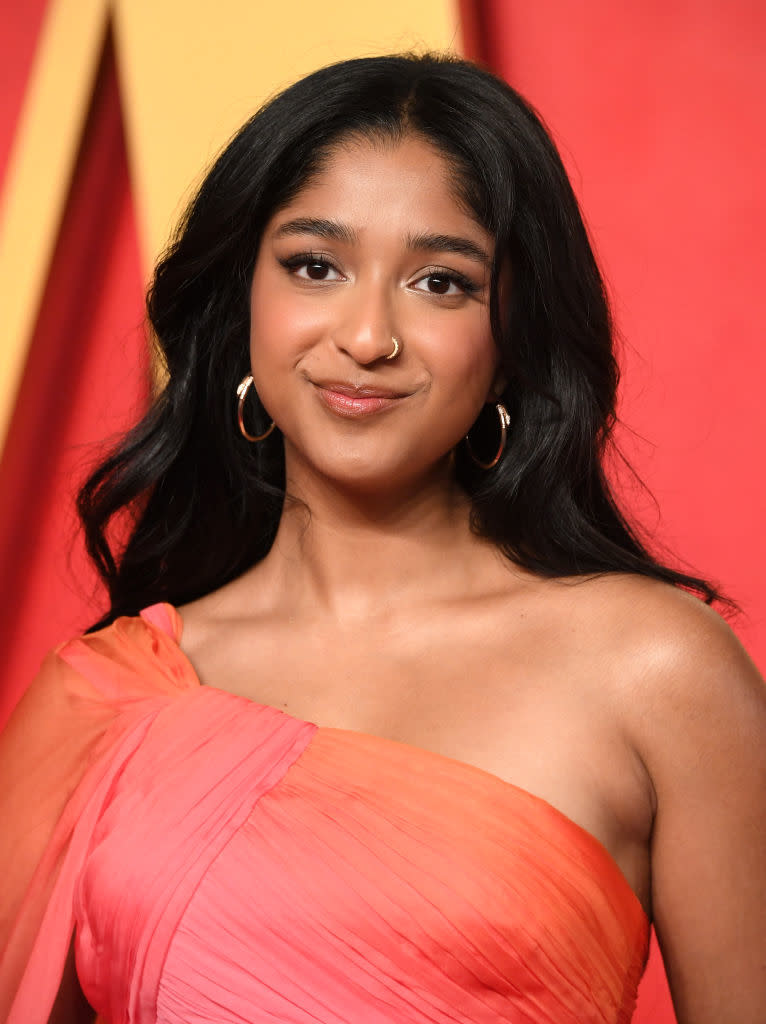 Maitreyi Ramakrishnan on the red carpet in a one-shoulder dress, smiling at the camera