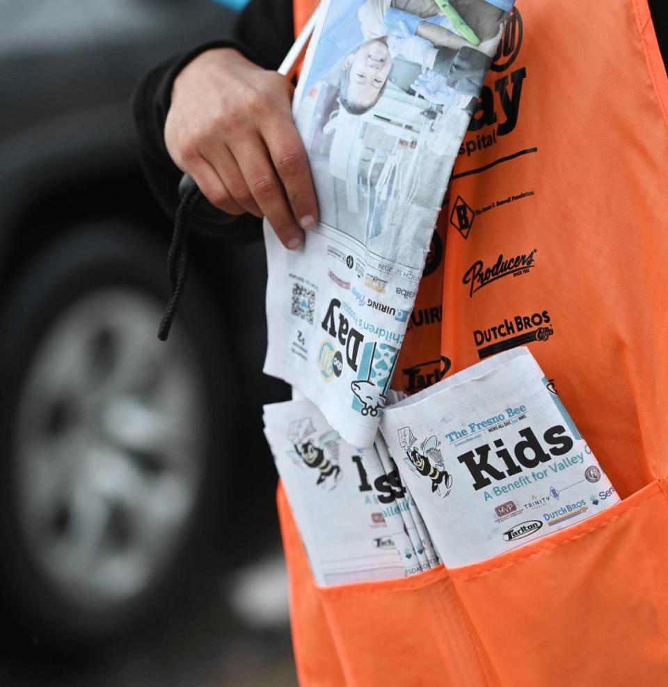 Pete Duarte holds a few copies of Kids Day newspapers while selling them with his daughter Penny at the corner of Friant and Audubon in Fresno on Tuesday, March 12, 2024. This is the first year hard copies of the paper are being sold on Kids Day since the COVID-19 pandemic in 2020.