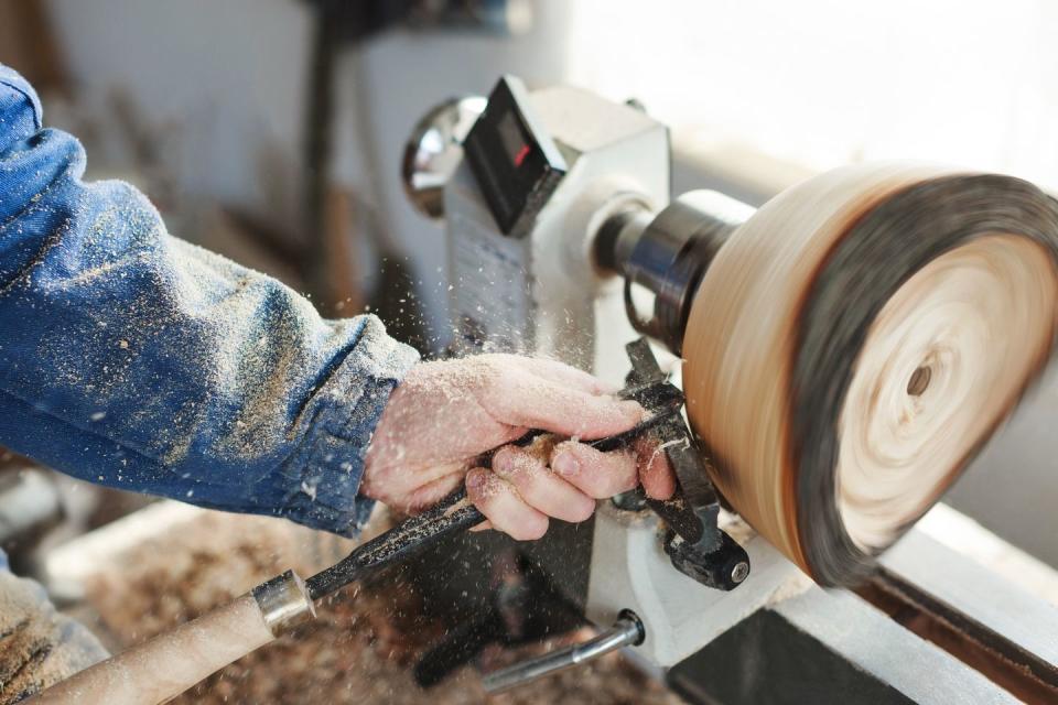 mans hands in blue jeans suit working with woodcarving machine, instruments and wood, shavings on table, close up, woodworking