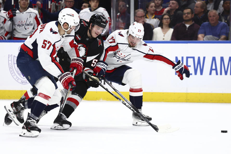 Buffalo Sabres left wing Eric Robinson (50) is checked by Washington Capitals defenseman Trevor van Riemsdyk (57) and defenseman Alexander Alexeyev (27) during the first period of an NHL hockey game Tuesday, April 2, 2024, in Buffalo, N.Y. (AP Photo/Jeffrey T. Barnes)