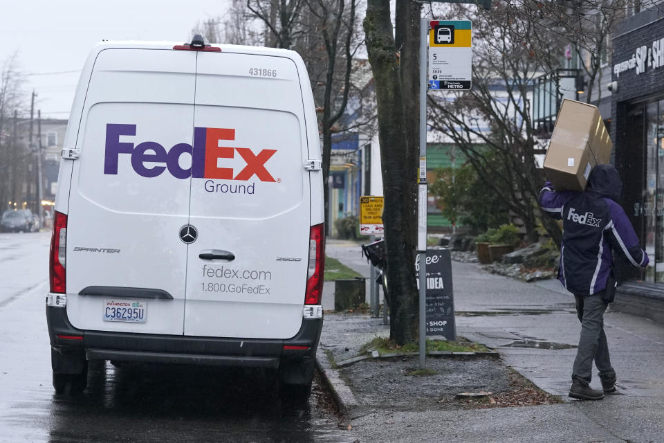 FILE - In this Tuesday, Dec. 8, 2020, file photo, a driver with FedEx carries a package away from a van, in Seattle. FedEx says its profit nearly tripled in its most recent quarter, despite winter weather that hobbled some of its facilities. Online shopping has surged during the pandemic as more people avoid going inside stores. That has made package delivery companies like FedEx in high demand. (AP Photo/Ted S. Warren, File)