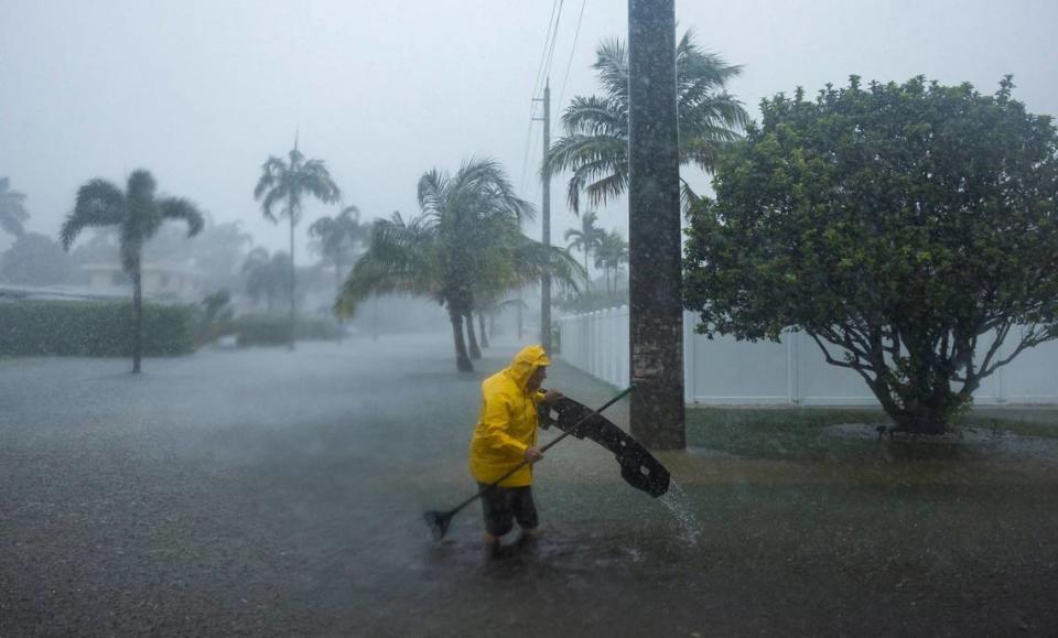 A man works to clear debris from a flooded street at the corner of Garfield Street and 14h Avenue as heavy rain floods the nearby neighborhood on Wednesday, June 12, 2024, in Hollywood, Florida.