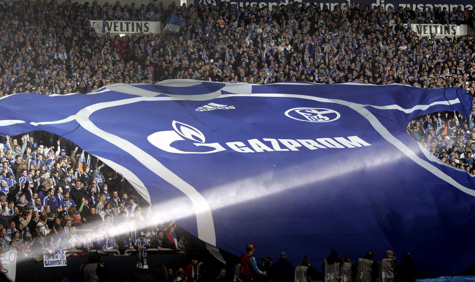 FILE - Soccer club FC Schalke 04 supporters unfold a giant team's jersey with the logo of Russian sponsor Gazprom, at the Veltins-Arena in Gelsenkirchen, Germany, on Jan. 20, 2007. The logo of Russian state-owned energy giant Gazprom is being removed from the jerseys of German soccer team Schalke following Moscow’s wide-ranging attack on Ukraine. Schalke said the logo would be replaced by lettering reading “Schalke 04” instead following what it called “recent developments.” A senior Gazprom executive had already quit the supervisory board of Schalke earlier Thursday, Feb. 24, 2022 after being a target of U.S. sanctions. (AP Photo/Martin Meissner, File)