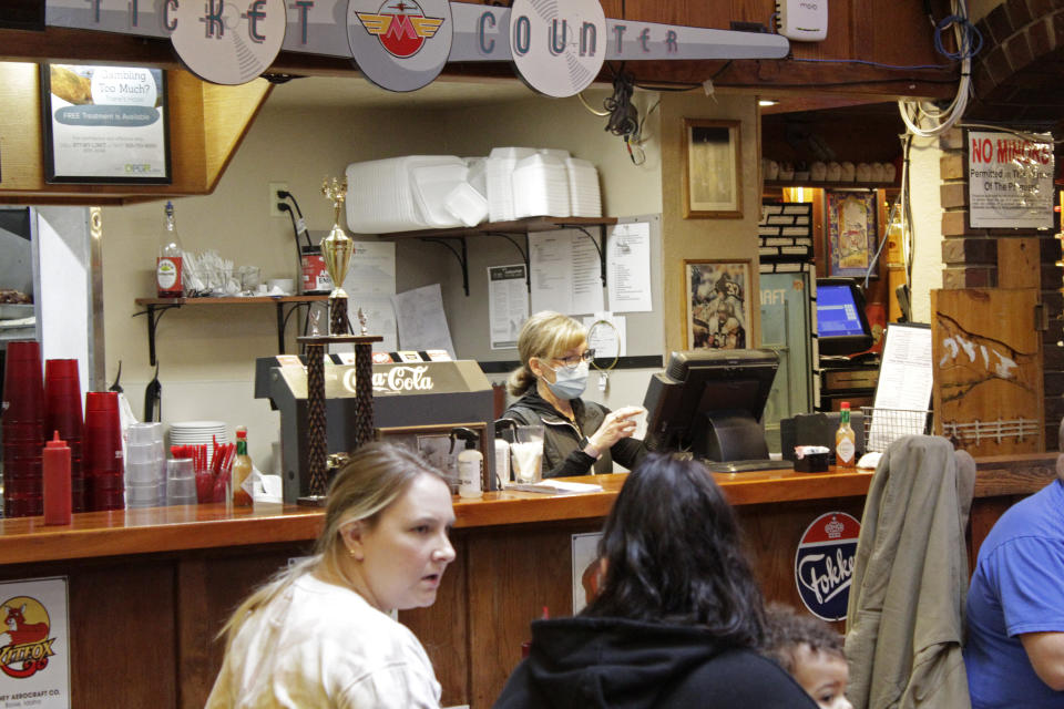 Restaurant co-owner Liz Mitchell works behind the bar at the Carver Hangar in Boring, Ore., on Jan. 6, 2021. As coronavirus deaths soar, a growing number of restaurants like Carver Hangar in states across the country are reopening in defiance of strict COVID-19 rules that have shut them down for indoor dining for weeks, or even months. (AP Photo/Gillian Flaccus)