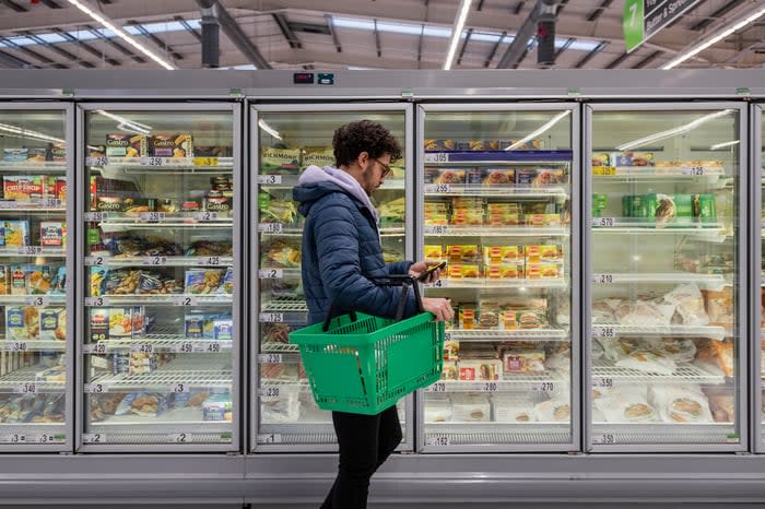 A person shopping in the freezer section of a grocery store.