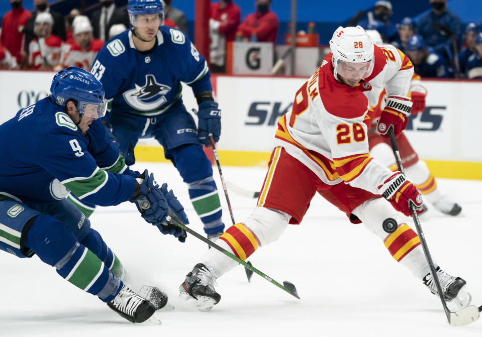 Vancouver Canucks center J.T. Miller (9) fights for control of the puck with Calgary Flames center Elias Lindholm (28) during the first period of an NHL hockey game Thursday, Feb. 11, 2021, in Vancouver, British Columbia. (Jonathan Hayward/The Canadian Press via AP)