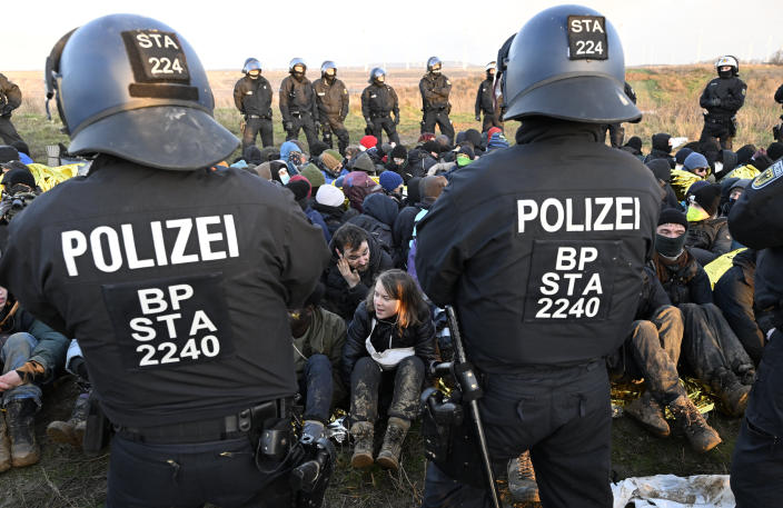 Police officers stand in front of a group of protesters, including Swedish climate activist Greta Thunberg, center bottom, on the edge of the Garzweiler II opencast lignite mine during a protest action by climate activists after the clearance of Luetzerath, Germany, Tuesday, Jan. 17, 2023. After the eviction of Luetzerath ended on Sunday, coal opponents continued their protests on Tuesday at several locations in North Rhine-Westphalia. (Roberto Pfeil/dpa via AP)