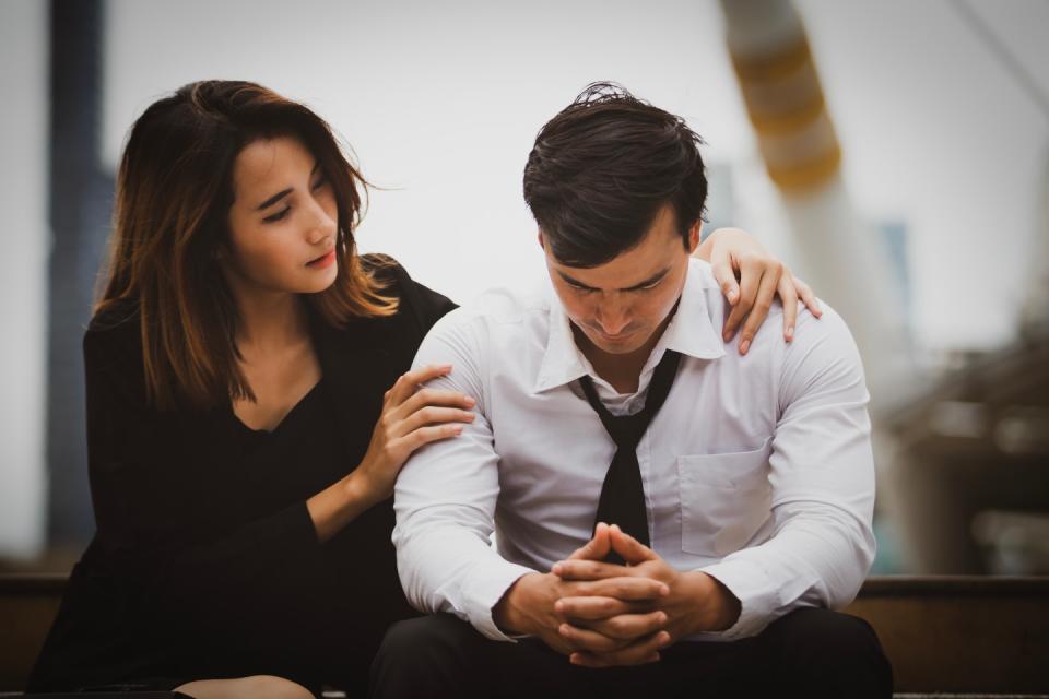 A woman puts her hands on a depressed man's shoulder while encouraging him.