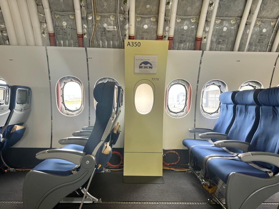Two rows of three blue chairs onboard a Boeing 777-9 test bed, with a small box showing the size of an A350 window by comparison