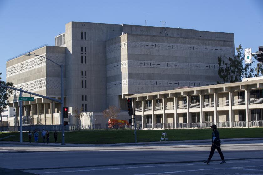 SANTA ANA, CA - December 15: A pedestrian walks past the Orange County Jail and Orange County Sheriff's Department Headquarters, right, in Santa Ana Tuesday, Dec. 15, 2020. An Orange County Superior Court judge ruled to halve the population of the county's jails to allow for more social distancing of inmates. The outbreak in the jails, which started last week, has escalated to 416 inmates, 37 of whom are newly booked prisoners, said Carrie Braun of the Orange County Sheriff's Department. (Allen J. Schaben / Los Angeles Times)