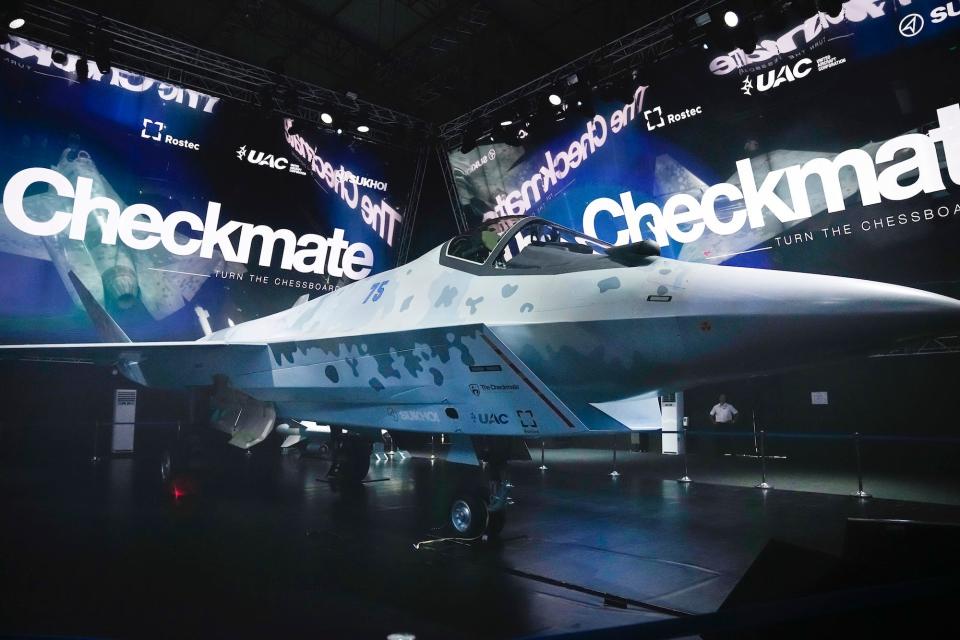 A prototype of Russia's new Checkmate stealth fighter jet in an event hall with large screens projecting "Checkmate" onto the walls.
