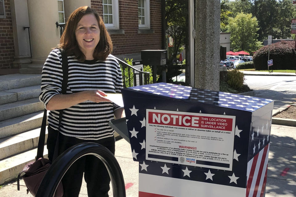 In this Oct. 3, 2020, photo provided by Paige Weber, she poses for a photo while casting her ballot in the presidential election in Decatur, Ga. Weber, who has diabetes, was worried about contracting the coronavirus at her polling place. She also was concerned about using the mail to return her ballot, so she opted for one of the more than two dozen drop boxes her county had set up. She was impressed with how easy — and safe — the process was. (Alasdair Young/Paige Weber via AP)