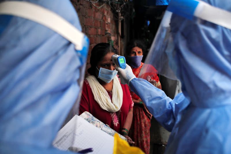 Healthcare worker checks the temperature of a woman using an electronic thermometer during a check up campaign for the coronavirus disease (COVID-19) at a slum area in Mumbai