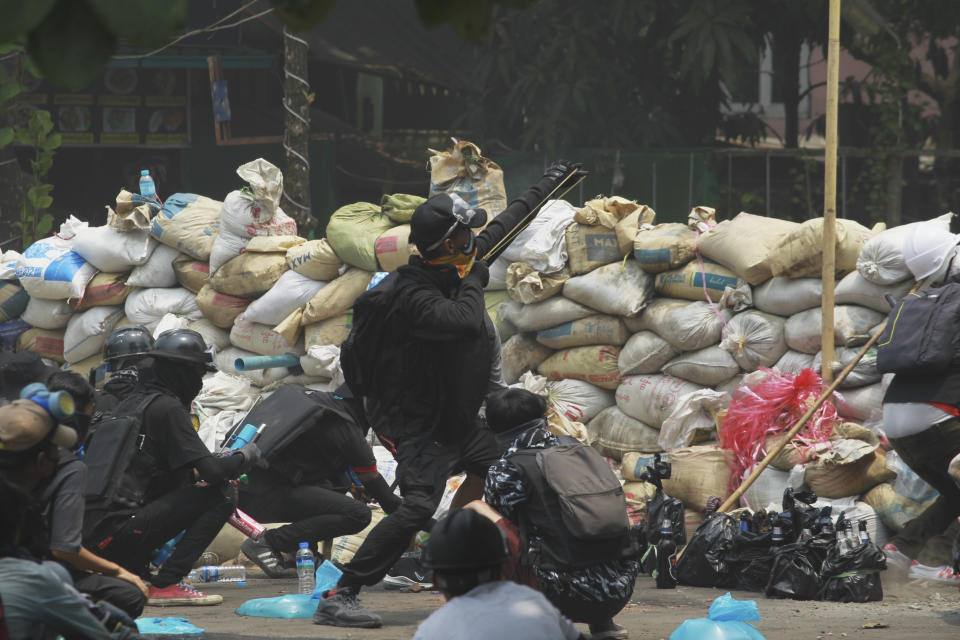 An anti-coup protester fires a slingshot at soldiers as they guard their position during a demonstration in Yangon, Myanmar on Tuesday, March 30, 2021. (AP Photo)