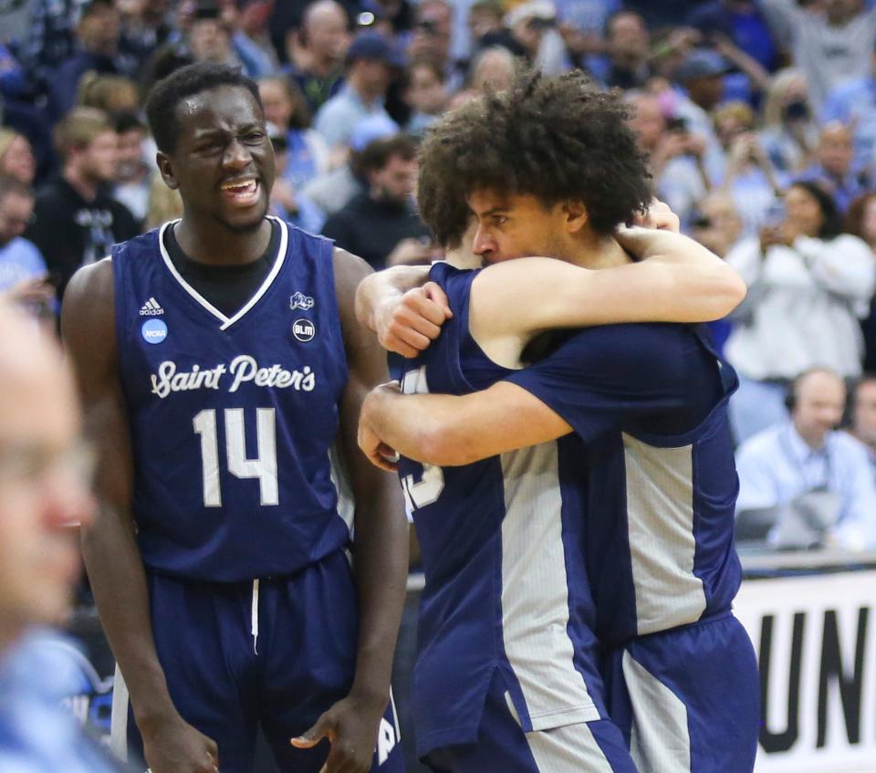 Saint Peter's Hassan Drame (14) celebrates as Doug Edert (center) and Daryl Banks III embrace after the Peacocks' 67-64 win against Purdue.