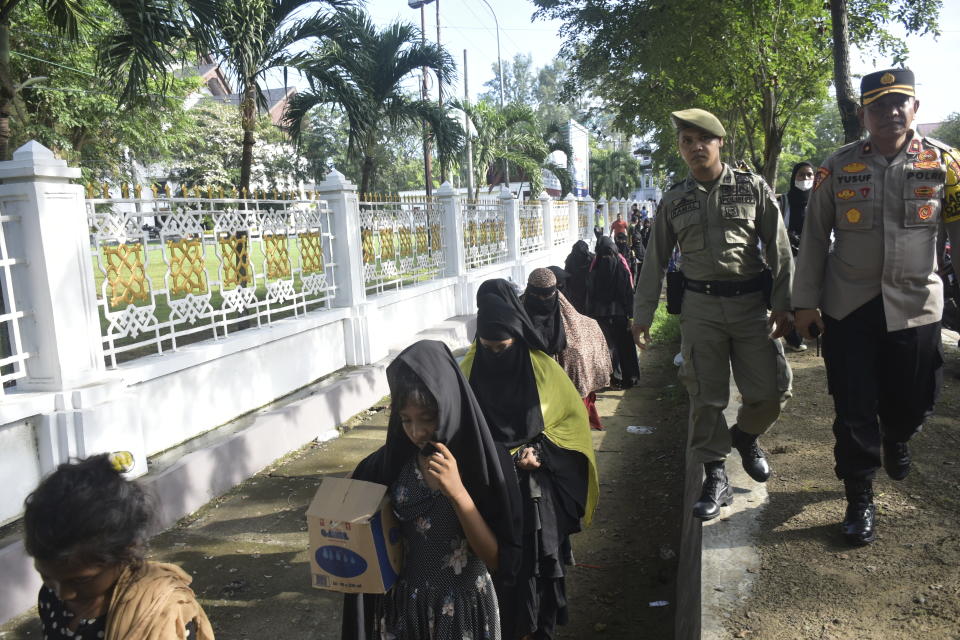 Police officers escort Rohingya refugees as they are removed rom outside the governor's office to a nearby park in Banda Aceh, Indonesia, Monday, Dec. 11, 2023. Two boats carrying hundreds of Rohingya Muslims, including emaciated women and children, arrived on Sunday at Indonesia's northernmost province of Aceh where they faced rejection from local communities who are protesting against the increasing numbers of refugees that have entered the region over the past few weeks. (AP Photo/Reza Saifullah)