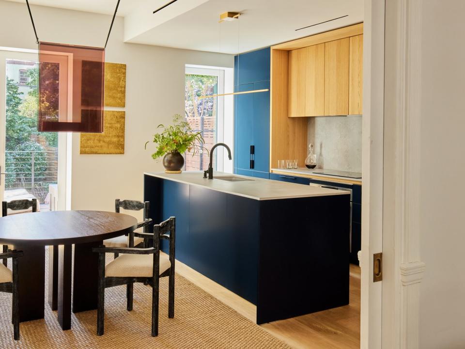 In the dining room, Guillerme et Chambron armchairs from Maison Gerard surround a CB2 table. The ceiling light is by Lambert & Fils. In the kitchen, rich blue cabinetry with wood details from GD Arredamenti is topped with a Caesarstone 