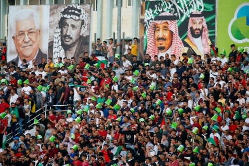 Football fans cheer below pictures of Palestinian president Mahmud Abbas, late Palestinian leader Yasser Arafat, and Saudi Arabia's King Salman and Crown Prince Mohammed bin Salman as Saudi Arabia played Palestine for the first time in the West Bank