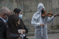 Violinist Antonio Hernandez plays for the relatives of COVID-19 victim Miryam Rodriguez, while they are gathered for prayer by the hearse that carries her remains to Serafin Cemetery, before cremation in Bogota, Colombia, Friday, June 18, 2021. Due to regulations to contain the new coronavirus, relatives cannot enter the cemetery. (AP Photo/Ivan Valencia)
