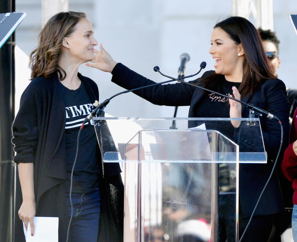 Natalie Portman and Eva Longoria smile and react at a podium.