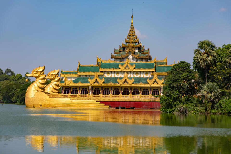 A golden barge on the water with a bow sculpture that's a golden-winged god bird, shaped as a pagoda