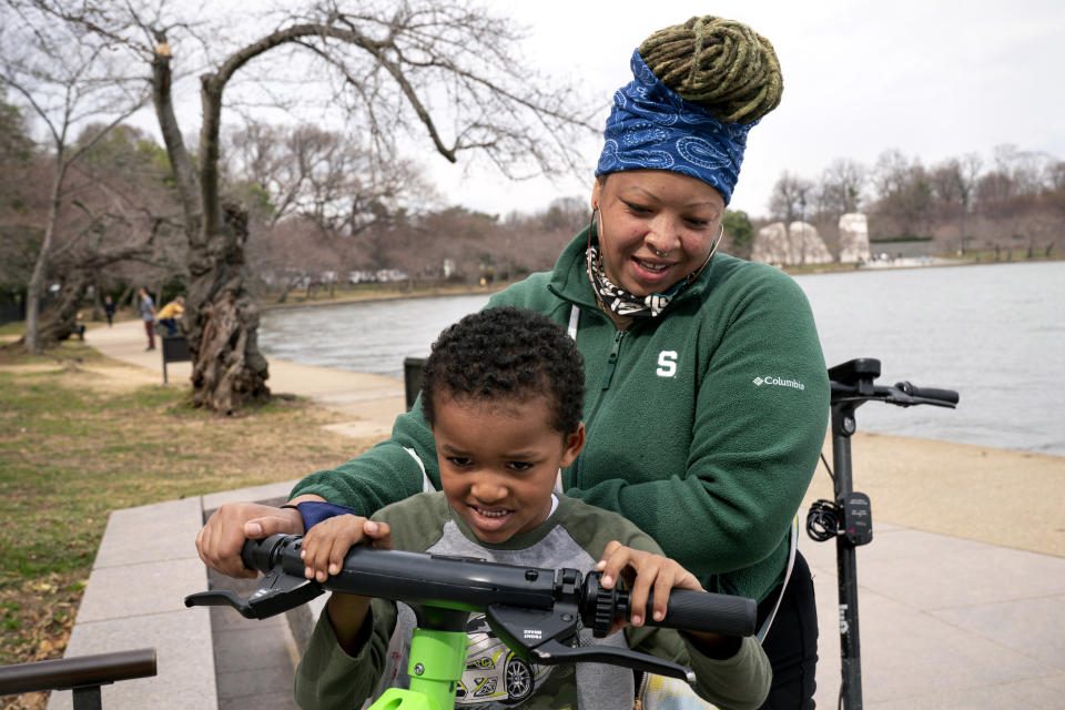 Ashley McCown, of Washington, helps her son, Kai Garrett, 5, pretend to ride an electric scooter on an unusually warm March day that reached into the low 80 degrees, Monday, March 7, 2022, along the tidal basin in Washington where the Cherry Blossom Trees are budding but not yet in bloom. McCown, who said she is from the Southeast neighborhood of Washington, "decided to take the day and run through the city because it's so nice out." (AP Photo/Jacquelyn Martin)