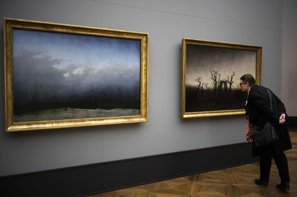 A woman inspects Caspar David Friedrich's painting 'Abby Among The Oaks' whis is displayed next to 'Monk By The Sea' during a press preview of the exhibition 'Caspar David Friedrich. Infinite Landscapes' at the Alte Nationalgalerie museum in Berlin, Wednesday, April 17, 2024. The exhibition marking the 250th birthday of Caspar David Friedrich and will run from April 19 until August 4, 2024. (AP Photo/Markus Schreiber)