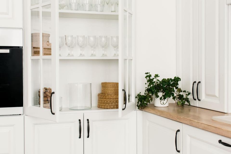 Opened white glass cabinet with clean dishes and decor. Scandinavian style kitchen interior. Organization of storage in kitchen.
