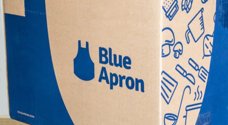 Image of the Blue Apron (APRN) logo on one of the company's branded cardboard boxes used for its deliveries. It features several images of vegetables and kitchen tools on the side, next to the logo.