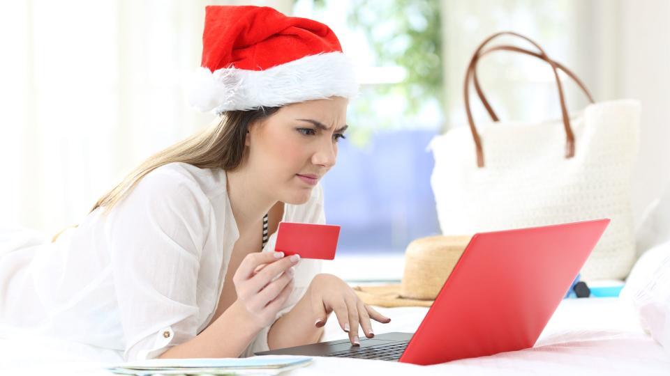 Confused woman paying online on christmas holidays lying on a bed in an hotel room.