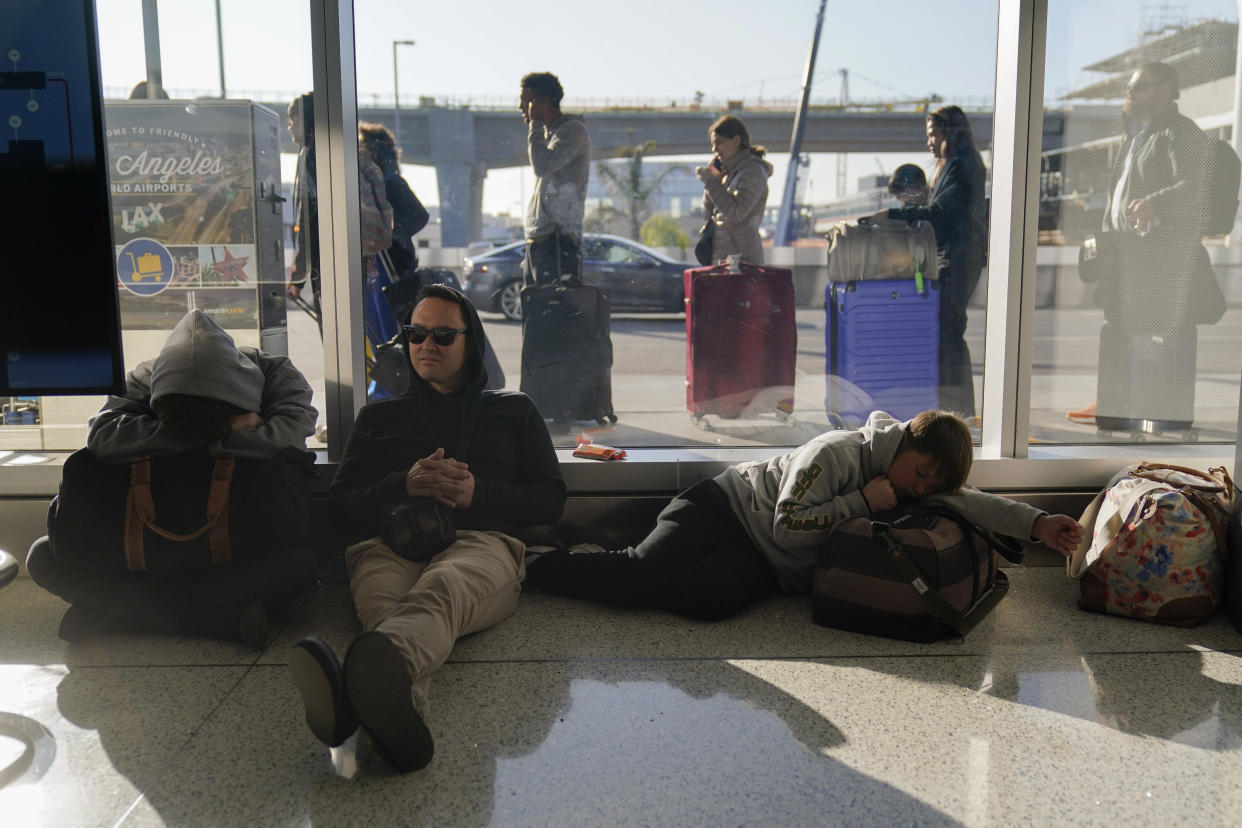 Rome DeGuzman sits on the floor of a terminal next to his two sons after missing a morning flight to Hawaii as travelers wait in line outside the building to check in at the Los Angeles International Airport in Los Angeles, Monday, Dec. 19, 2022. Forecasters are warning of treacherous holiday travel and life-threatening cold for big parts of the nation. (AP Photo/Jae C. Hong)