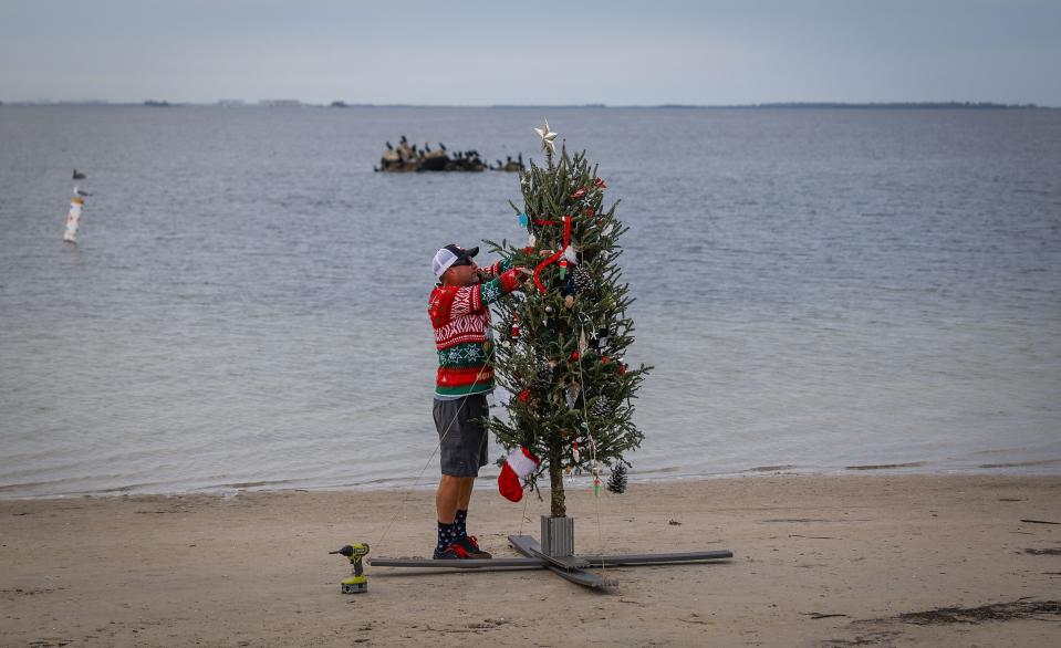 Mike Womack, 52, puts the final touches on a Christmas tree along Sunset Beach Sunday, Dec. 24, 2023 in Tarpon Springs, Fla. For the past nine years Womack has set up a tree along the beach for local residents to enjoy. (Chris Urso/Tampa Bay Times via AP)