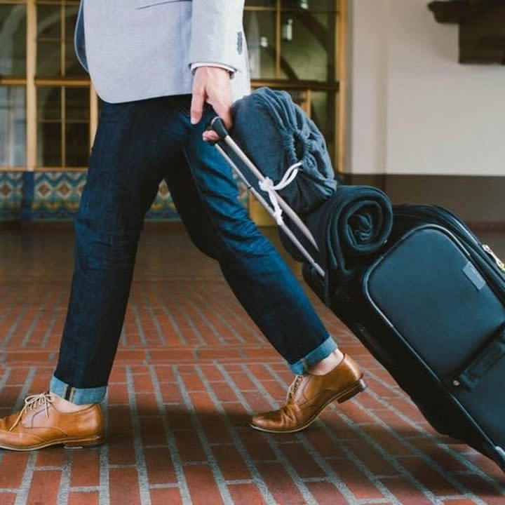 traveler carrying the rolled up blanket on top of their suitcase