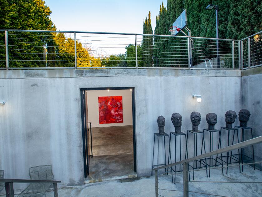 A subterranean space holds sculptures and a door opening into a room with a painting visible on the wall