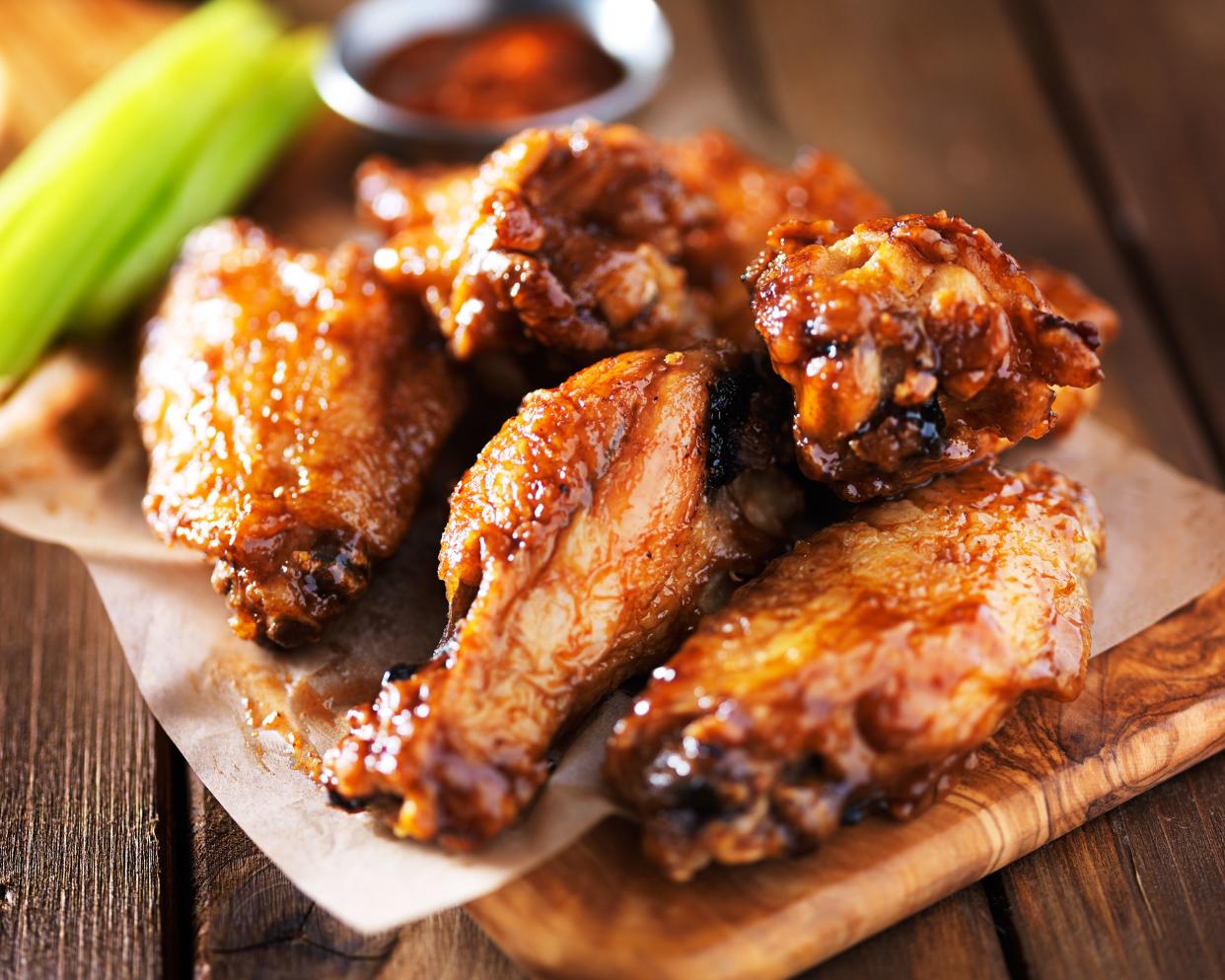 Selective focus of several baked buffalo wings on a wooden cutting board with dipping sauce and celery on a rustic wooden table