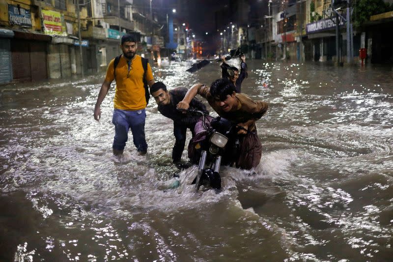 FILE PHOTO: Boys push their motorcycle after it was stopped on a flooded street, following heavy rains during the monsoon season in Karachi