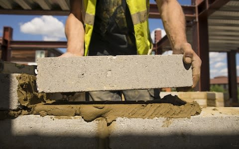 A construction worker lays a block onto mortar during building work at a residential site in the Tower Hamlets district of London - Credit: Jason Alden/&nbsp;Bloomberg