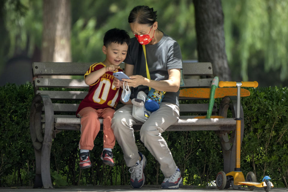 Una mujer con mascarilla y un niño observan un celular sentados en una banca en un parque público en Beijing, el 2 de junio de 2022. (AP Foto/Mark Schiefelbein, Archivo)