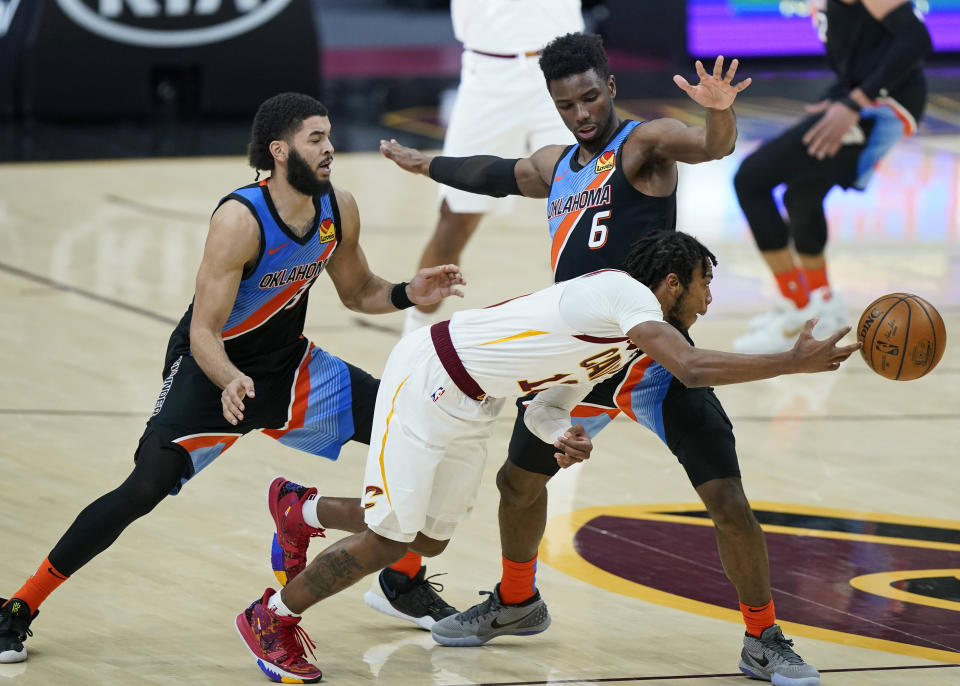 Cleveland Cavaliers' Darius Garland, front, passes against Oklahoma City Thunder's Hamidou Diallo, right, as Kenrich Williams, left, defends in the second half of an NBA basketball game, Sunday, Feb. 21, 2021, in Cleveland. (AP Photo/Tony Dejak)