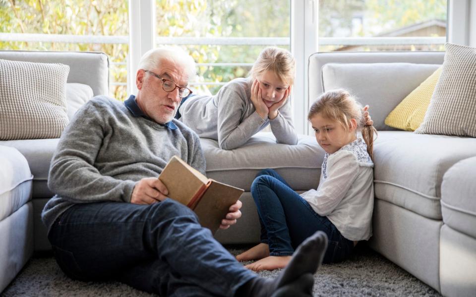 Two girls and grandfather reading book in living room