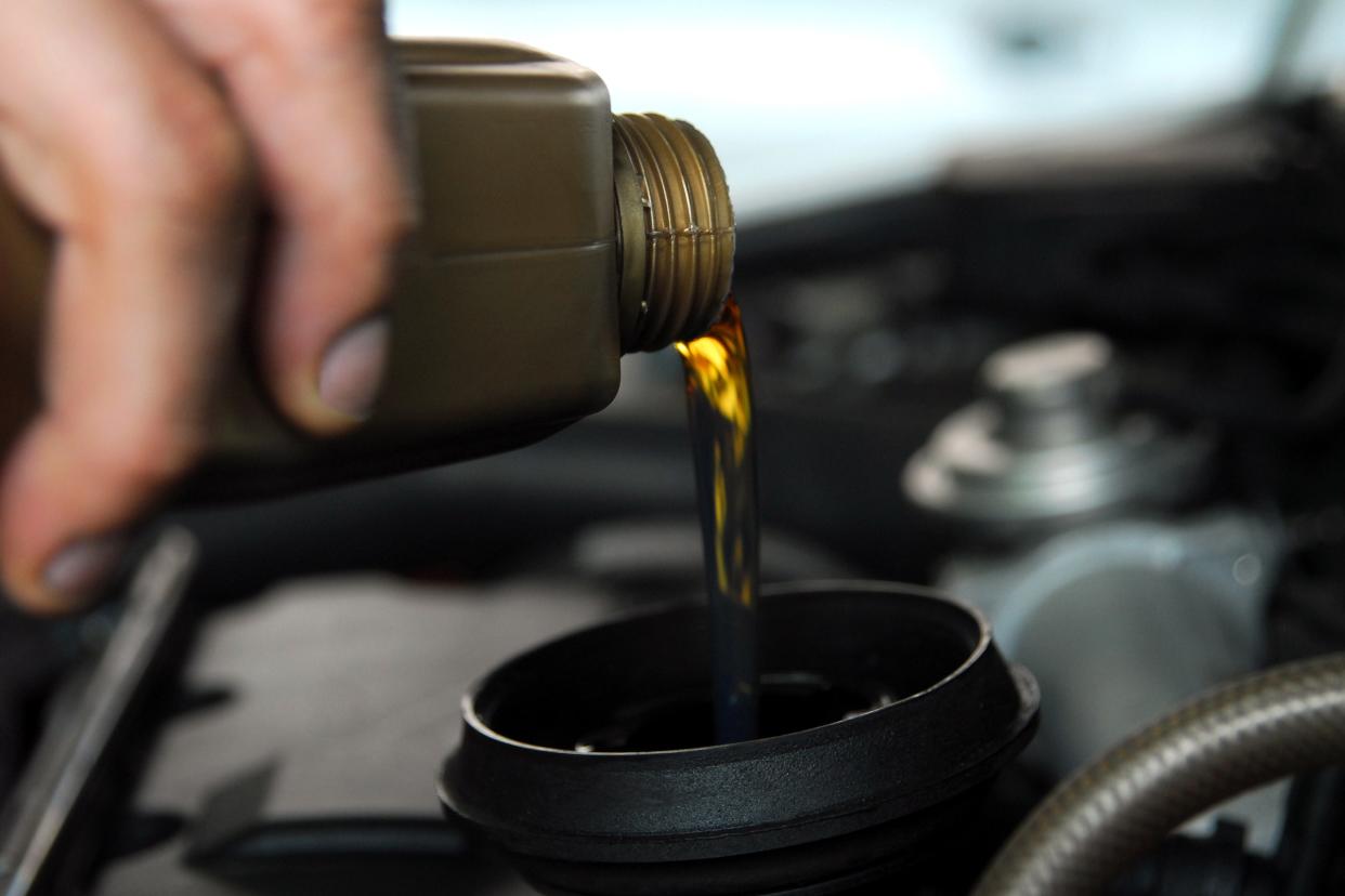 hand adding oil to car