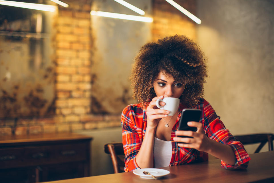 A woman drinking coffee while looking at her smartphone