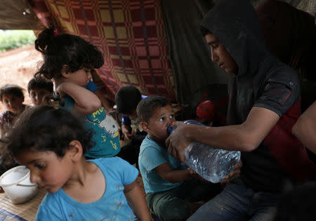 A displaced Syrian boy from the al-Ahmed family drinks water with the help of another family member in an olive grove in the town of Atmeh, Idlib province, Syria, May 16, 2019. REUTERS/Khalil Ashawi