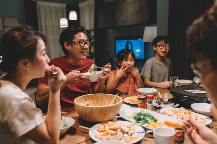 Family of five eating dinner together at a dining table, enjoying various dishes and interacting cheerfully